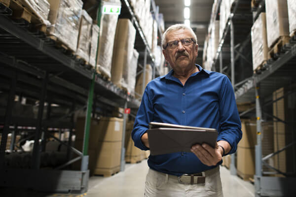 Self employed man with workers comp insurance with binder walking down an aisle in a warehouse