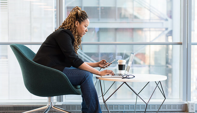 Black woman working at a coffee table with laptop and phone researching retirement plans