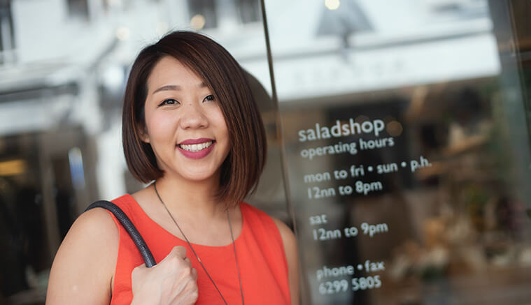 Asian woman standing outside of her salad shop