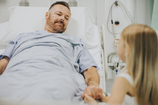 Man on oxygen in hospital bed with young daughter holding his hand