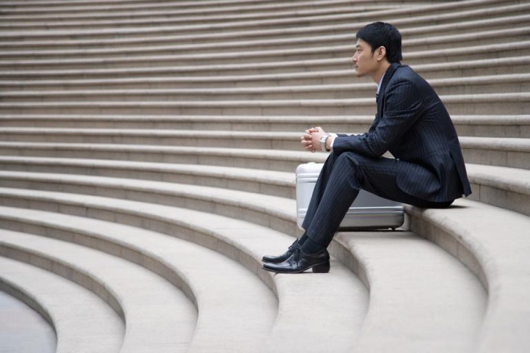 man sitting on staircase with a suitcase after being laid off
