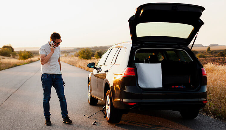 Man on the side of the road with an SUV with a flat tire calling for help using the Safeguard Discount membership