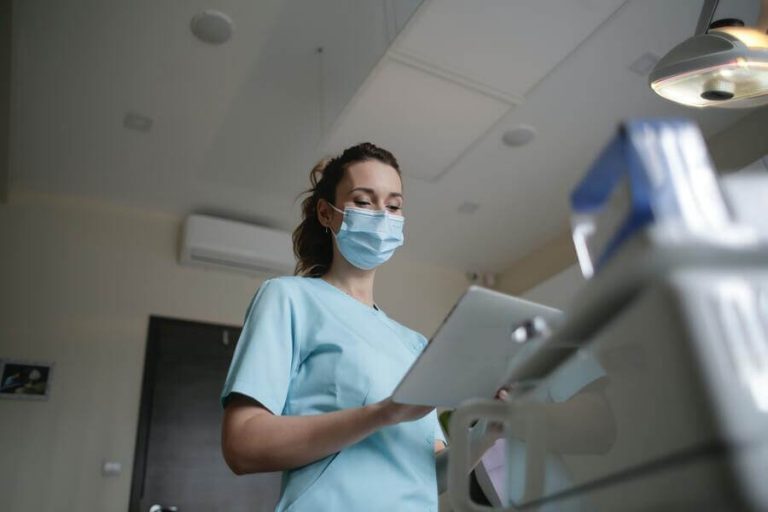 Female nurse wearing mask while writing on clipboard.