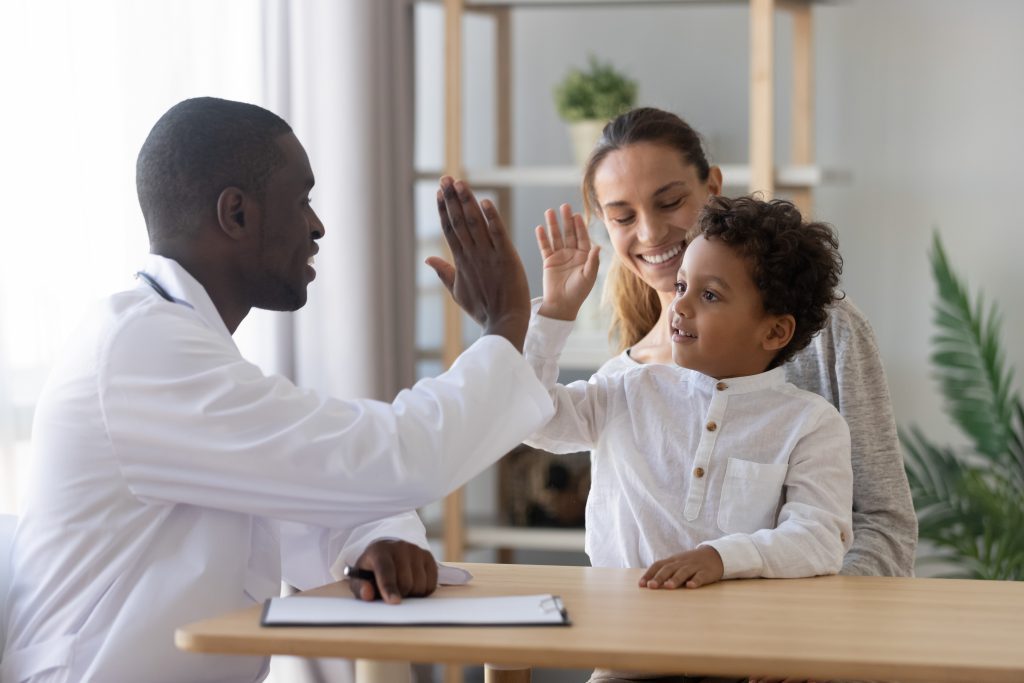 Black Pediatrician give high five to mixed race child sitting on mother's lap