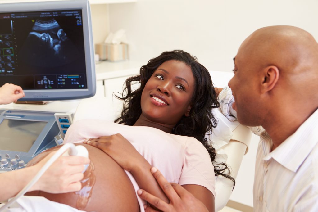 Black pregnant mother looks lovingly into her black husbands eyes while they find out the sex of their unborn baby