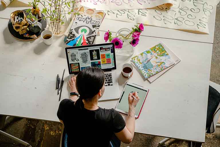 Graphic Designer Working On Table with Laptop and Drawing Materials