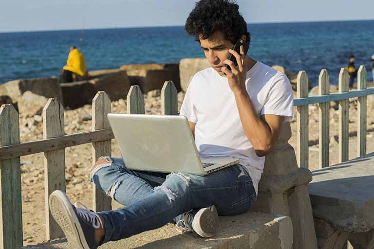 Egyptian freelance writer talking on cell phone on a bench near beach