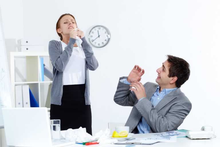 Woman standing up over man about to sneeze sick at work