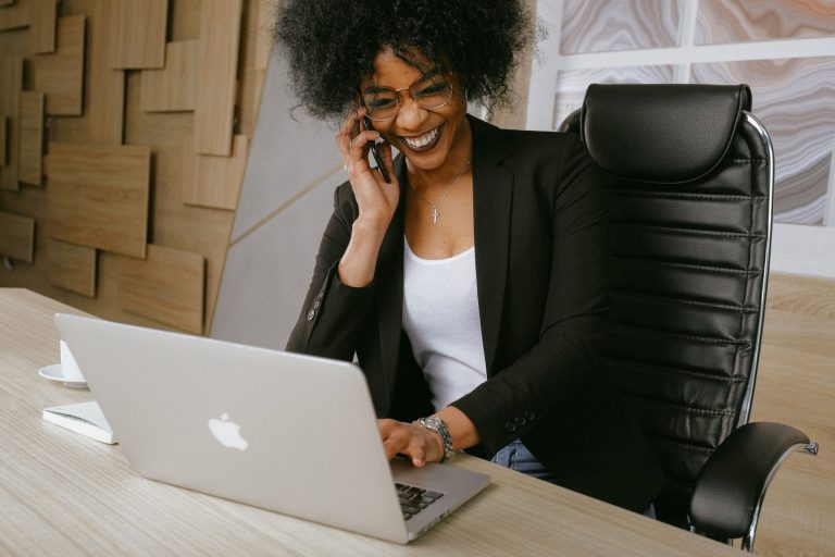 black female on cell phone talking to client in front of laptop