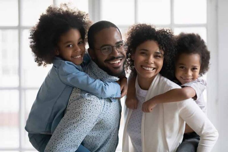 Black family with two small children. Mom and dad each giving child a piggy back ride