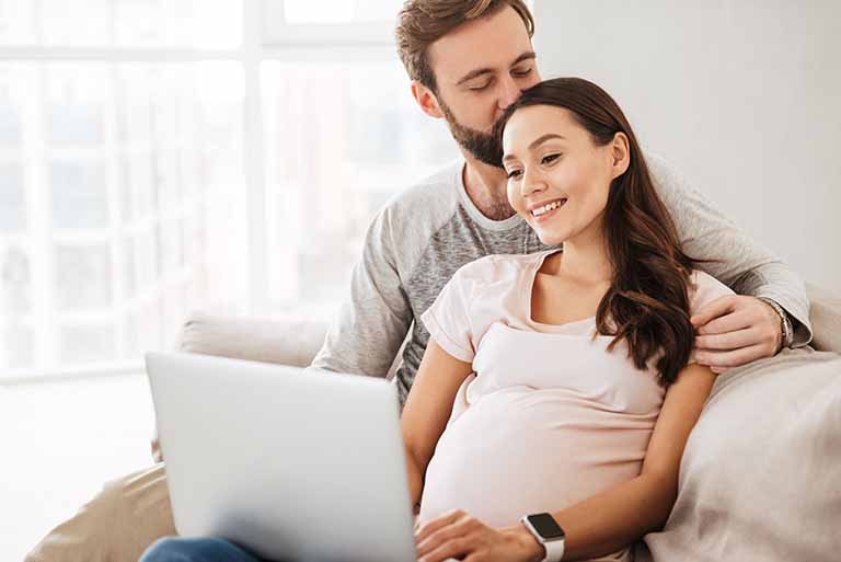 Expectant mother and father sit on sofa reading about health insurance through the Affordable Care Act