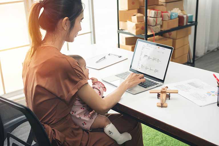 Asian mother researching health insurance terms on laptop holding daughter