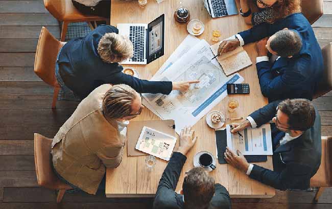 Men and women looking at a blueprint sitting around a conference table