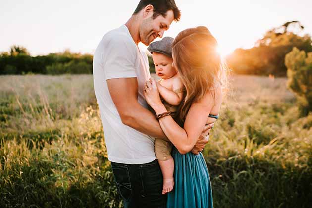 mother and father with baby in field with sun behind them