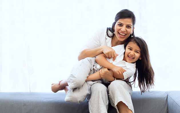 Indian mother and daughter snuggling on sofa