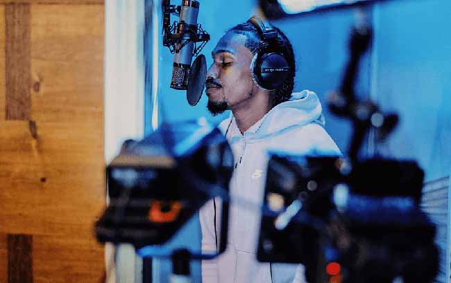 Black recording artist in studio singing into microphone wearing headphones