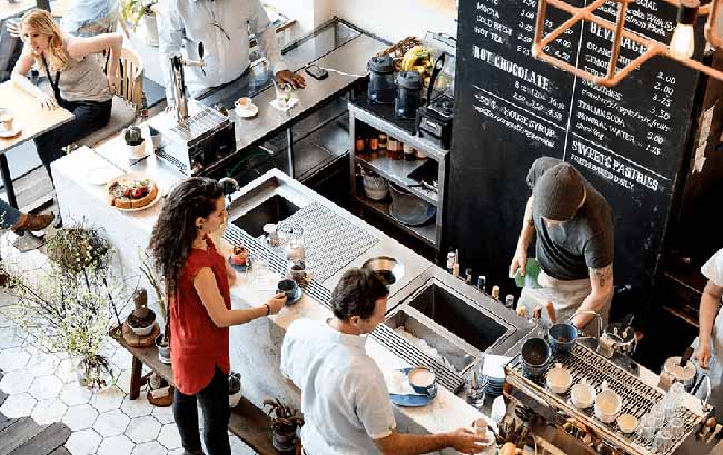 Birdseye view of a coffeeshop counter with a barista and two customers drinking coffee