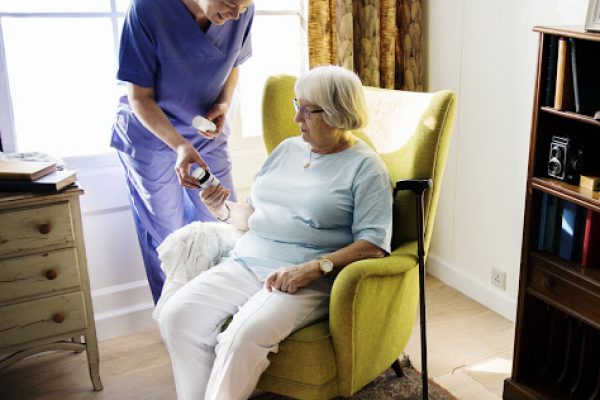 Nurse is taking care of a senior woman home nurse giving water to retired 65 year old lady